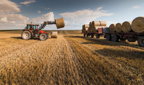 Stock-throughput-Transit Tractor loading bails of hay onto a semi truck in field