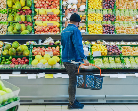 Back view of a man standing in produce aisle holding a basket